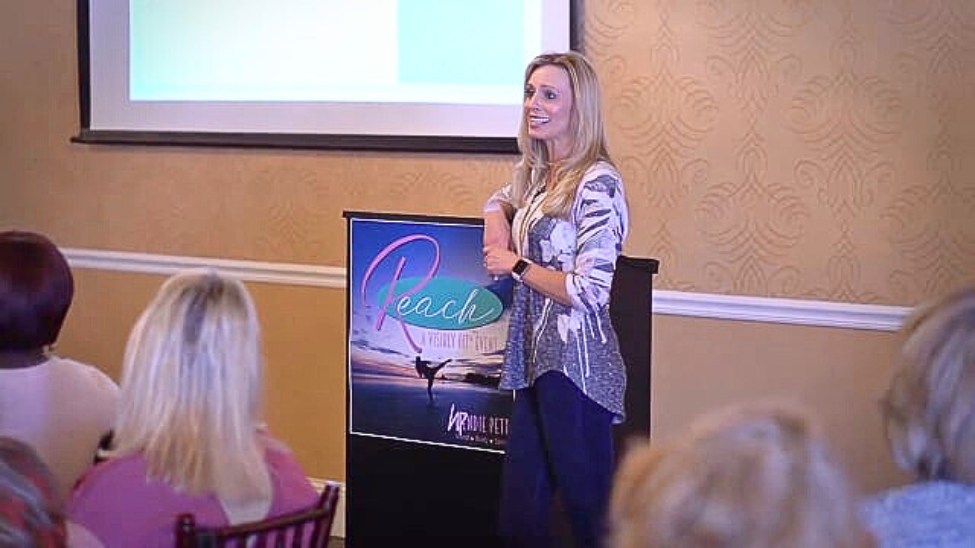 Wendie Pett, ND smiling next to a monitor displaying REACH at a Visibly Fit™ event.